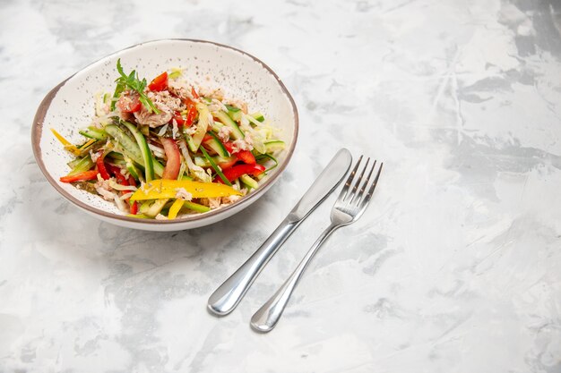 Above view of chicken salad with vegetables and cutlery set on stained white surface