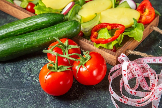 Above view of chopped vegetables fresh tomatoes with stem meter and cucumbers on a wooden tray on mix colors surface