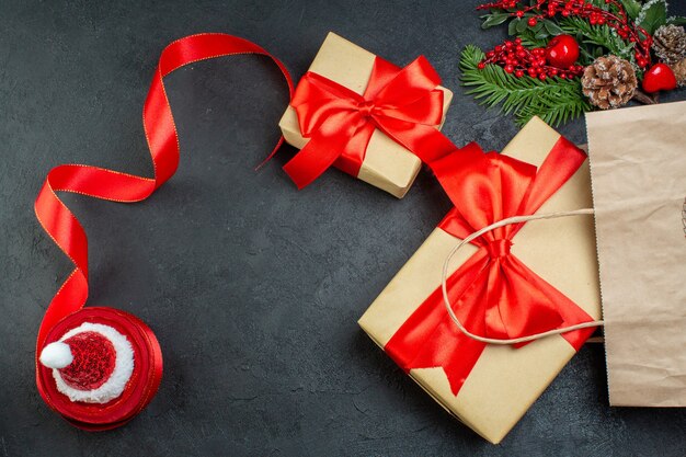 Above view of Christmas mood with beautiful gifts fir branches conifer cone red ribbon on dark background