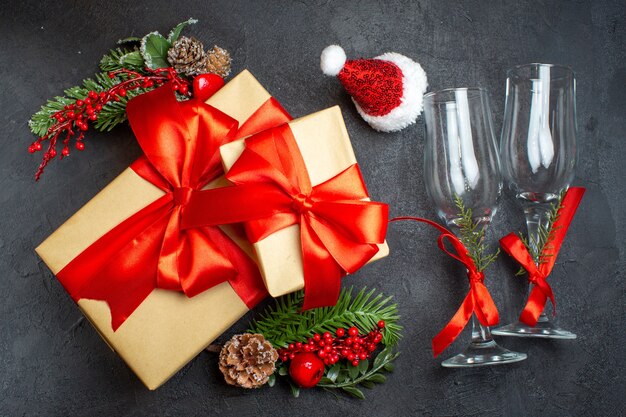 弓形のリボンとモミの枝の装飾アクセサリーと美しい贈り物とクリスマス気分のビューの上に暗い背景にサンタクロースの帽子ガラスのゴブレット針葉樹の円錐形