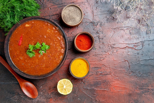 茶色のボウルに古典的なトマトスープと混合色のテーブルにさまざまなスパイスのビューの上