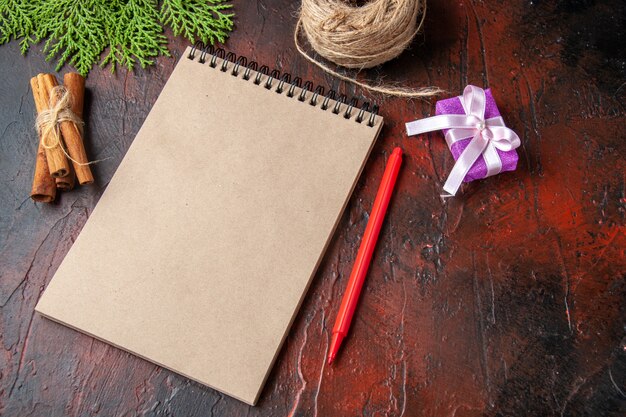 Above view of closed notebook cinnamon limes and gift on dark background