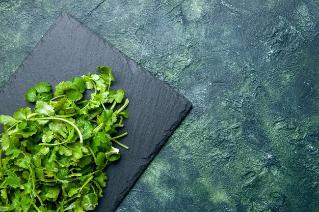 Above view of coriander bundle on wooden cutting board on the right side on green black mixed colors table with free space