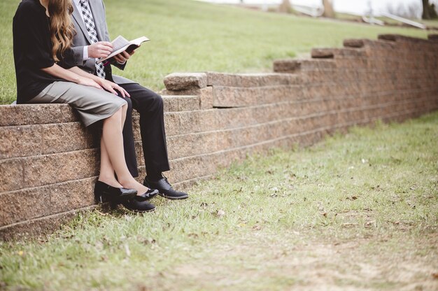 View of a couple wearing formal clothes and reading a book while sitting in a garden