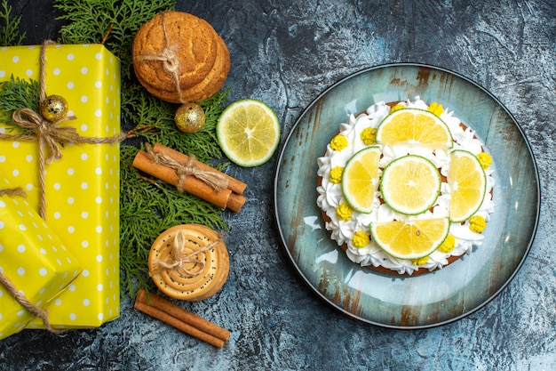 Sopra la vista di una deliziosa torta cremosa e scatole regalo gialle rami di abete limone e cannella lime su sfondo scuro Foto Gratuite