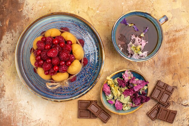 Above view of a cup of hot herbal tea soft cake with fruits and flowers chocolate bars