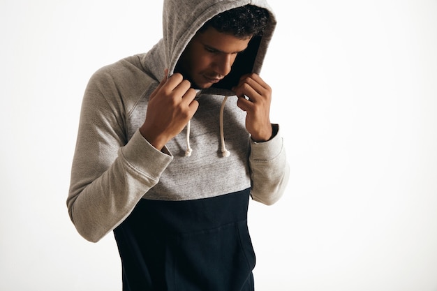 Free photo view of dark skinned man looking down, wears his hood with his hands, side view