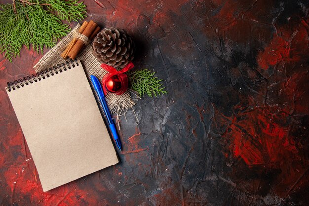 Above view of decoration accessories conifer cone fir branches cinnamon limes and notebook on dark background