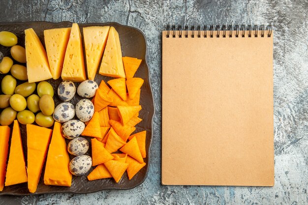 Above view of delicious best snack for wine on brown tray and notebook on ice background