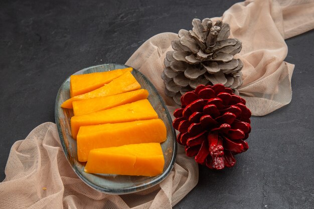 Above view of delicious chees slices and conifer cones on a towel on a black background