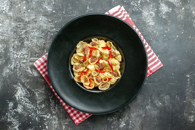 Above view of delicious conchiglie with vegetables on a plate and knife on red stripped towel on gray background