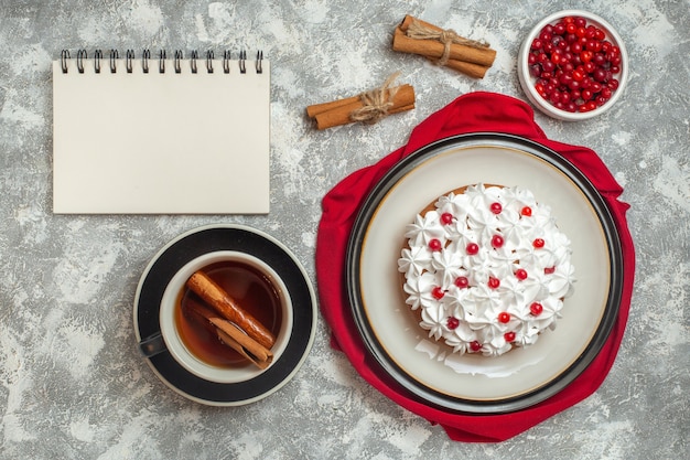 Выше вид восхитительного сливочного торта, украшенного фруктами, на красном полотенце и чашке черного чая.