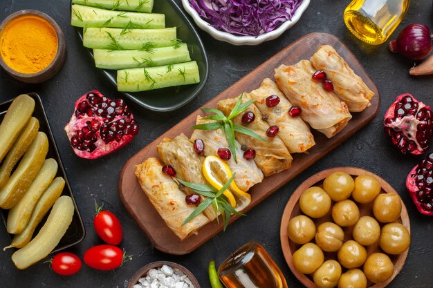 Above view of delicious dolma torshi cucumber yellow ginger pomegranate tomatoes fallen oil bottle on black wall