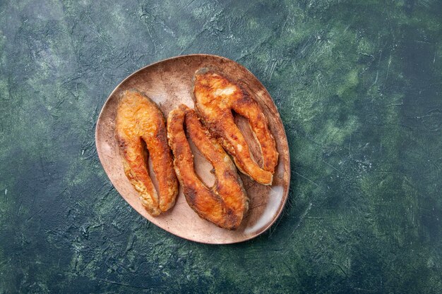 Above view of delicious fried fish on a brown plate on mix colors table with free space