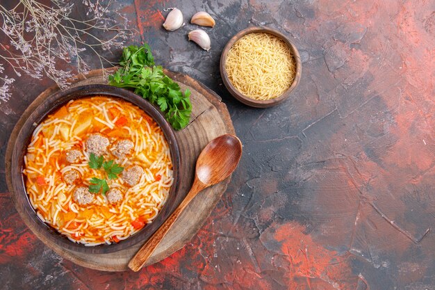 Above view of delicious noodle soup with chicken on wooden cutting board greens garlic spoon on dark background