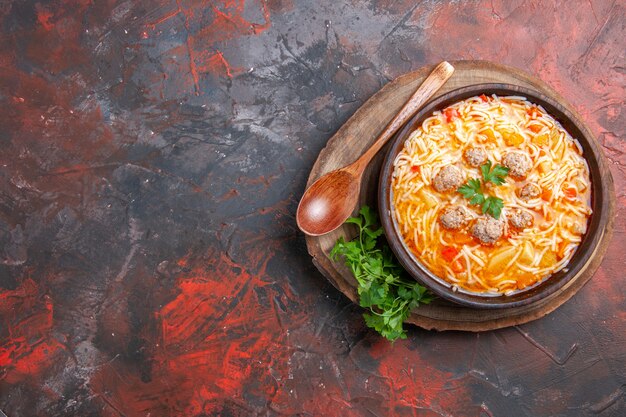 Above view of delicious noodle soup with chicken on wooden cutting board greens spoon on dark background