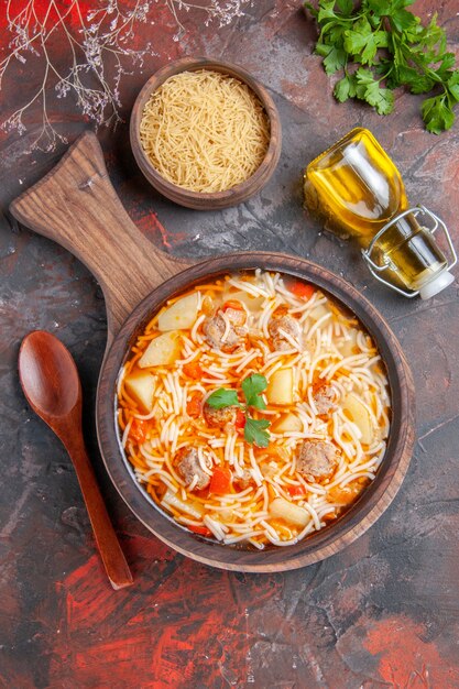 Above view of delicious noodle soup with chicken on wooden cutting board oil bottle and greens on dark table