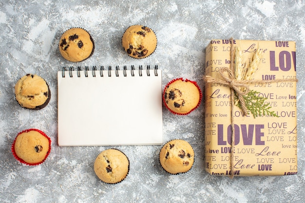 Выше вид вкусных маленьких кексов с шоколадом вокруг ноутбука и подарка с любовной надписью на поверхности льда