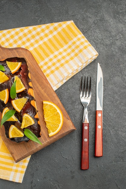 Выше вид на вкусные мягкие пирожные на деревянной доске и нарезанные апельсины с листьями на темном столе