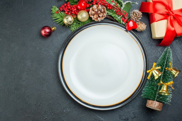 Above view of dinner plate christmas tree fir branches conifer cone gift box on the left side on black background