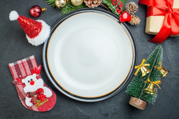 Above view of dinner plate christmas tree fir branches conifer cone gift box santa claus hat christmas sock on black background