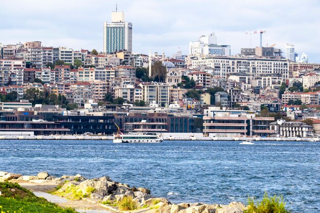 View of a district with residential and high modern buildings in Istanbul, Bosphorus Strait with boats, people resting on the shore, Turkey