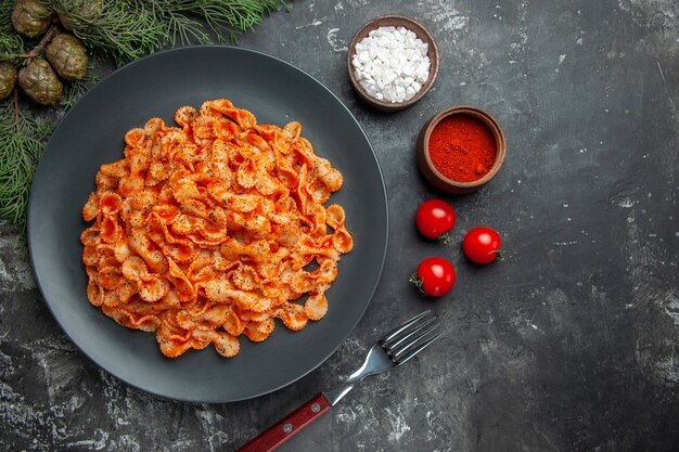 Above view of easy pasta meal for dinner on a black plate and fork on different spices and tomatoes on a dark background