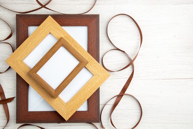 Above view of empty wooden picture frames in different sizes around ribbon on white