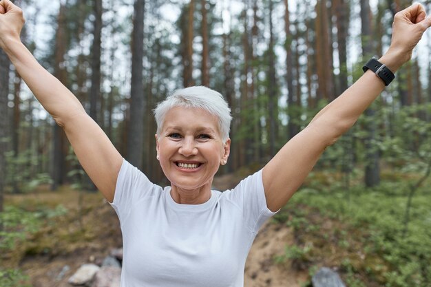 view of energetic confident middle aged woman runner raising hands, rejoicing at success as she broke her own record