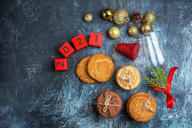 Above view of fallen glass goblet with red ribbon and decoration accessories next to stacked cookies numbers on dark background