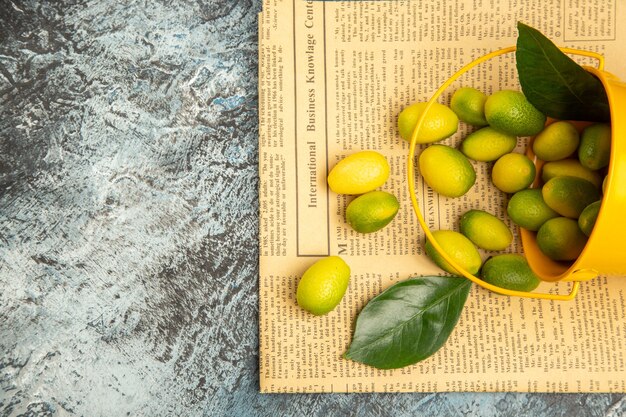 Above view of fallen yellow bucket with fresh kumquats on newspapers on gray table