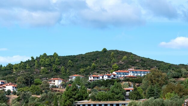 Вид на несколько зданий, выполненных в идентичном стиле, на холме, покрытом пышной зеленью в Уранополисе, Греция