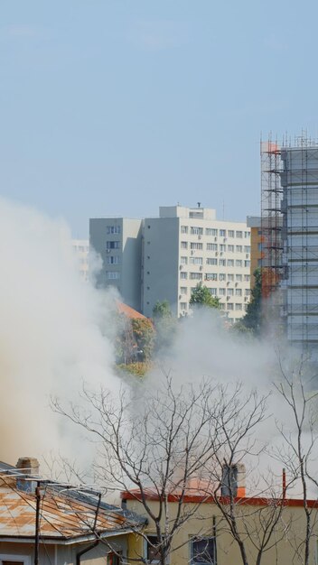 都市景観の燃えている家から出る炎の眺め。消防士が危険な煙を水で消そうとしている間、煙とスモッグが建物から出て行きます。