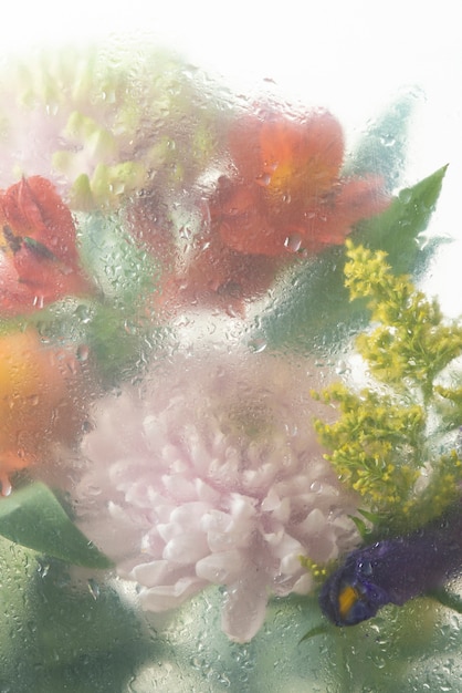 View of flowers through condensed glass with water drops