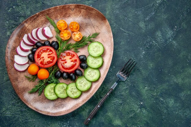 Above view of fresh chopped vegetables olives in a brown plate and fork on green black mixed colors table