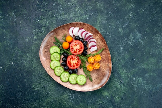 Free photo above view of fresh chopped vegetables olives kumquats in a brown plate on green black mixed colors table