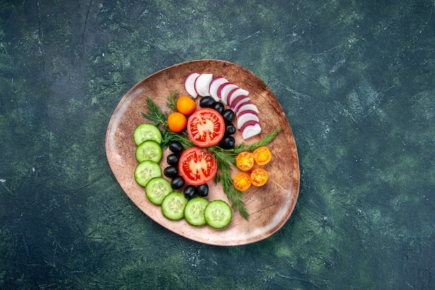 Выше вид свежих нарезанных овощей кумкватов оливок в коричневой тарелке на зеленом черном столе смешанных цветов