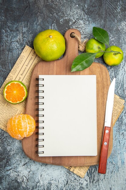 半分の形にカットされた木製のまな板の葉と灰色の背景の新聞にナイフでノートブックと新鮮な柑橘系の果物のビューの上