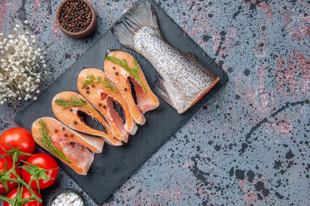 Free photo above view of fresh cut raw fishes green on dark color tray spices on blue black mix colors table with free space