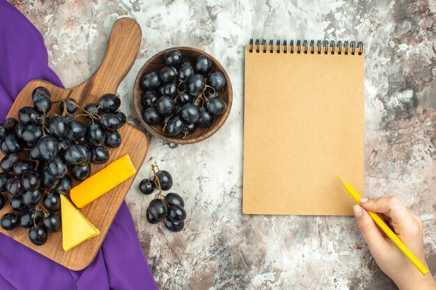 Above view of fresh delicious black grape bunch and cheese on wooden cutting board