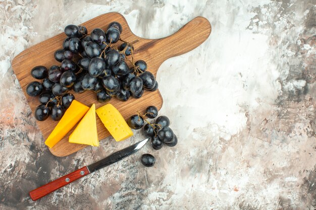木製のまな板と混合色の背景のナイフの新鮮なおいしい黒ブドウの束とさまざまな種類のチーズのビューの上