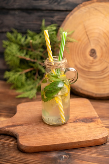 Above view of fresh detox water in a glass served with tubes on a wooden cutting board on a brown table