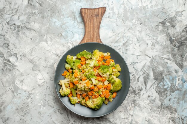 Above view of fresh and healthy vegetable salad on wooden cutting board on white table