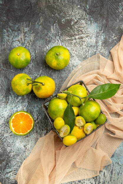 Above view of fresh kumquats and lemons in a black basket on towel and four lemons on gray background