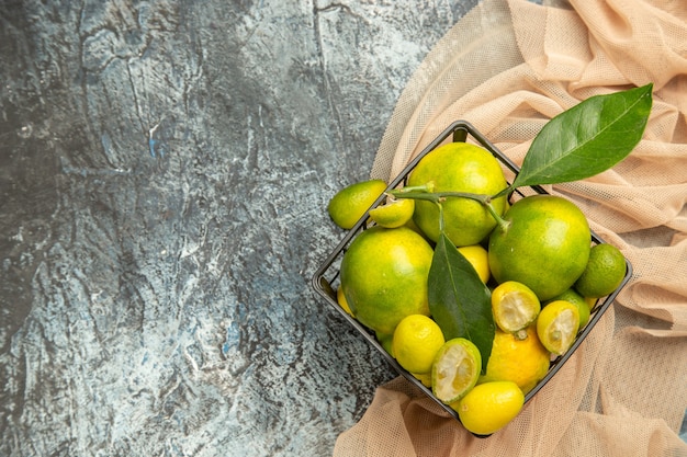 Above view of fresh kumquats and lemons in a black basket on towel on gray background