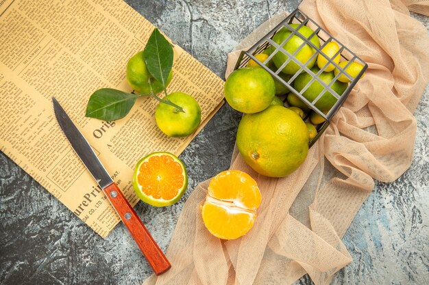 Above view of fresh lemons in a fallen black basket on towel knife and newspaper on gray table