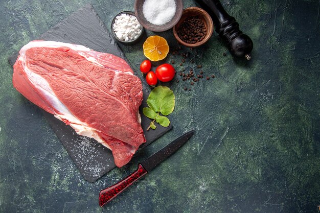 Above view of fresh raw red meat on black tray pepper salt lemon wooden hammer on dark color background