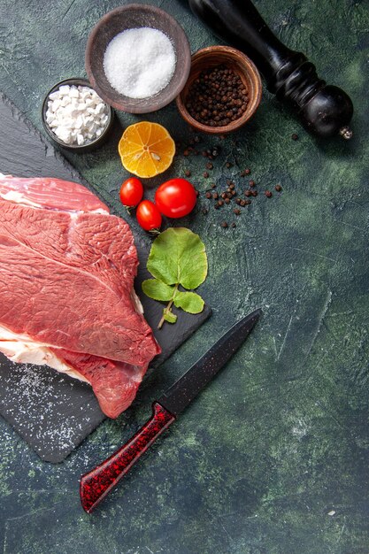 Above view of fresh raw red meat on black tray pepper salt lemon wooden hammer knife on dark color background
