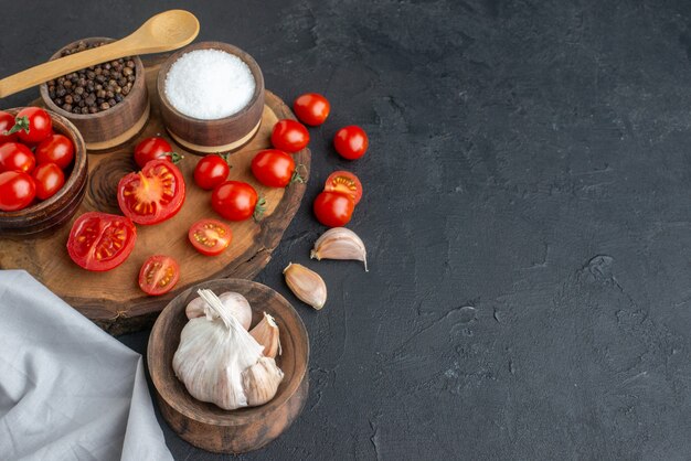 Above view of fresh tomatoes and spices on wooden board white towel garlics on black surface