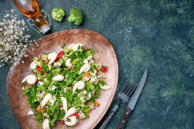 above view fresh vegetable salad inside elegant plate with cutlery on dark blue background